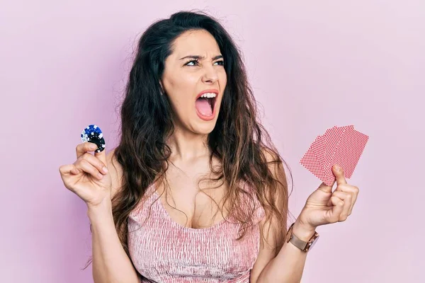 Elinde kumarhane fişleri ve kartlarla poker oynayan genç İspanyol kadın kızgın ve öfkeli çığlıklar atıyor, öfkeyle bağırıyor. öfke ve agresif konsept. 