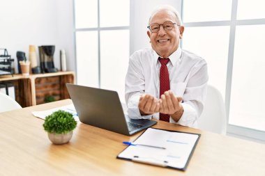 Ofiste çalışan kıdemli bir adam, elinde avuçlarıyla gülümseyen ve el hareketi yapan bilgisayar dizüstü bilgisayar kullanıyor. Bekleme ve koruma 