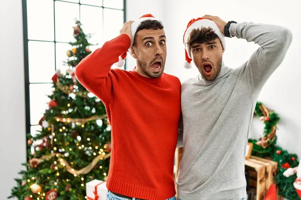 若いですゲイカップル立ってクリスマスツリー身に着けています帽子クレイジーと恐怖で手で頭 恐怖と驚きのショックでオープン口 — ストック写真