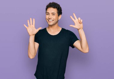 Siyah tişört giyen genç ve yakışıklı bir adam 8 numaralı parmaklarıyla onu gösterirken kendinden emin ve mutlu bir şekilde gülümsüyor.. 