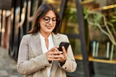 Genç İspanyol iş kadını şehirde akıllı telefon kullanarak mutlu gülümsüyor..