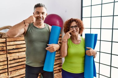 Orta yaşlı çift ellerinde yoga minderi tutarken, parmakları burunları ve yüzleri birbirine dönük, neşeli gülümsüyorlar. güzellik konsepti 
