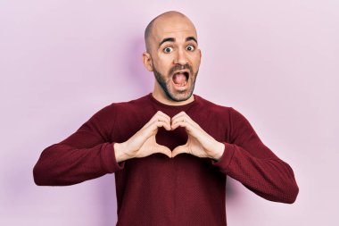 Genç kel adam kalp sembolü yapıyor elleri çılgın ve şaşkınlık dolu bir şekilde başarıyı kutluyor gözleri açık heyecanla haykırıyor. 