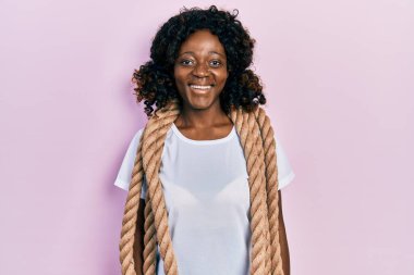 Genç Afro-Amerikan kadın savaş halatıyla antrenman yapıyor. Pozitif ve mutlu görünüyor. Kendine güvenen bir gülümsemeyle dişlerini gösteriyor. 