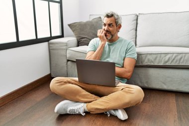 Orta yaşlı İspanyol bir adam oturma odasında dizüstü bilgisayar kullanıyor. Elleri ağızdan tırnak yerken gergin ve stresli görünüyor. anksiyete. 