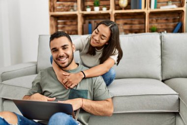 Evde dizüstü bilgisayar kullanarak mutlu gülümseyen genç Latin çift..