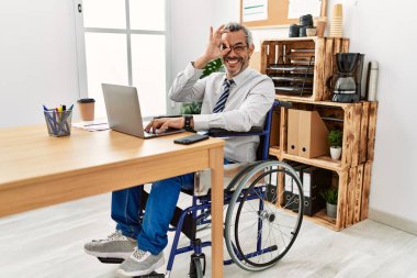 Orta yaşlı, ispanyol bir adam ofiste çalışıyor. Tekerlekli sandalyede oturuyor. El hareketleriyle gülümsüyor.. 