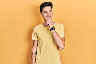 Sarı günlük tişört giyen genç İspanyol adam kameraya kendinden emin bakıyor kollarını kavuşturmuş ve çenesini kaldırmış gülümsüyor. Olumlu düşünmek. 