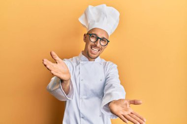 Profesyonel aşçı üniforması giyen kel bir adam kameraya bakıp sarılmak için kollarını açmış gülümsüyor. Mutluluğu kucaklayan neşeli bir ifade.. 