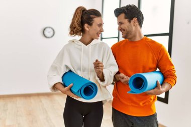 Genç İspanyol sporcu çift gülümseyerek yoga minderi tutuyor spor merkezinde duruyor..