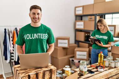 Bağışta gönüllü tişört giyen genç bir adam ve kadın dişlerini gösteren kendine güvenen bir gülümsemeyle ayakta ve mutlu görünüyorlar. 