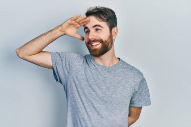 Sakallı, günlük gri tişörtlü, mutlu ve tebessüm eden beyaz bir adam. arama kavramı. 