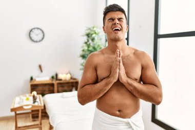 İspanyol asıllı genç adam spa merkezinde üstsüz duruyor. Elleri bağlı yalvarıyor ve dua ediyor. Yüzünde umut ifadesi var. Yalvarıyor. 