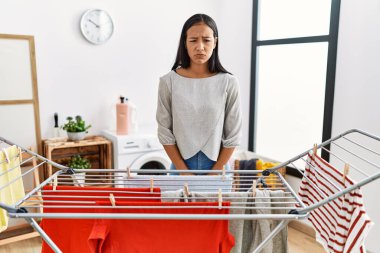 Genç İspanyol kadın çamaşır ipine yeni çamaşır koyuyor şüpheci ve gergin, sorun yüzünden somurtuyor. negatif kişi. 