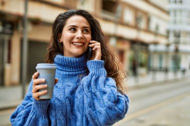Genç İspanyol kadın akıllı telefondan konuşuyor ve şehirde kahve içiyor..