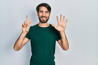 Gündelik beyaz tişört giyen genç İspanyol adam yedi numarayı gösterip işaret ederken kendinden emin ve mutlu bir şekilde gülümsüyor.. 