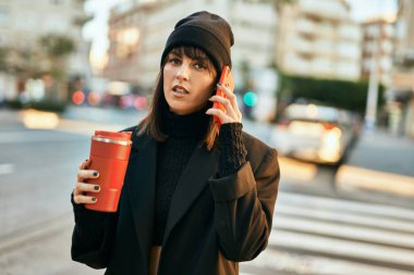 Genç İspanyol kadın akıllı telefondan konuşuyor ve şehirde kahve içiyor..