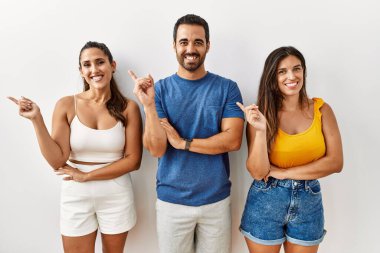 Bir grup İspanyol asıllı genç, izole edilmiş arka planda, yüzünde büyük bir gülümsemeyle kameraya el ile işaret ederek duruyorlar.. 