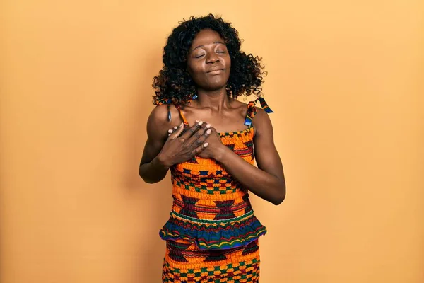 若いアフリカ系アメリカ人の女性は 目を閉じて胸に手を笑顔で伝統的なアフリカの服を着て 顔に感謝のジェスチャー 健康の概念 — ストック写真