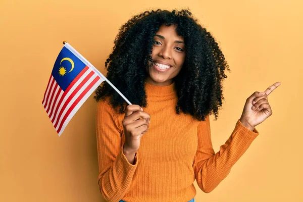 Африканская Американка Афроволосами Держащая Флаг Малайзии Улыбается Показывая Рукой Пальцем — стоковое фото