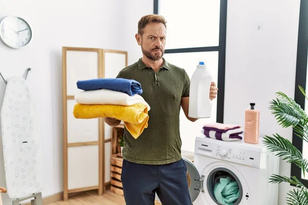 中年男子拿着干净的洗衣房和洗涤剂瓶子 毫无头绪 表情混乱 怀疑概念 — 图库照片