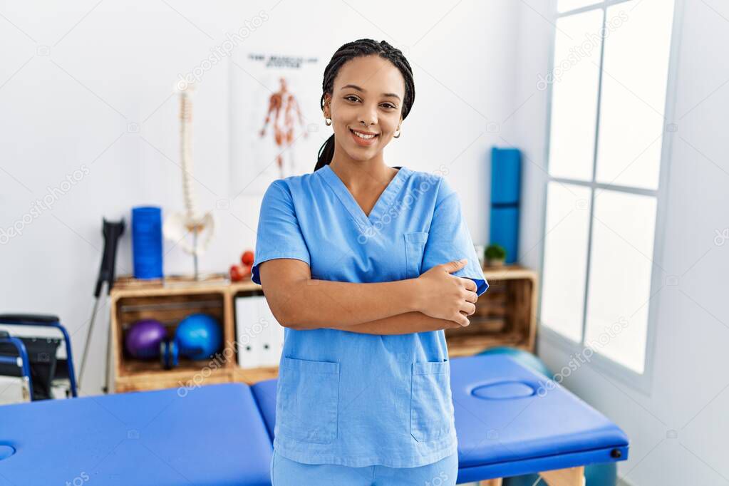 Young african american woman working at pain recovery clinic happy face smiling with crossed arms looking at the camera. positive person. 