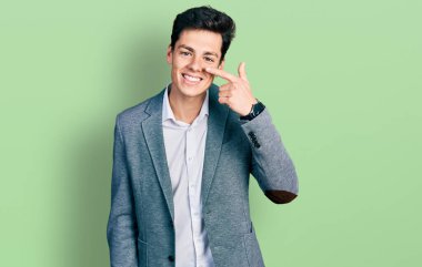 İş kıyafetleri giymiş genç İspanyol adam, el ve burun parmaklarıyla işaret ediyor, neşeyle gülümsüyor. güzellik konsepti 