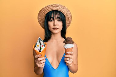 Kâküllü, mayo giyen, elinde iki dondurma külahı tutan esmer bir kadın. Yüzünde ciddi bir ifadeyle rahatlamış. Basit ve doğal bir şekilde kameraya bakıyorsun.. 