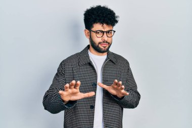 Sakallı, iğrenç bir ifade takınan, tiksindirici bir ifade takınan, tiksinti reaksiyonu yüzünden tiksinti duyan genç bir Arap. Eller havada. 