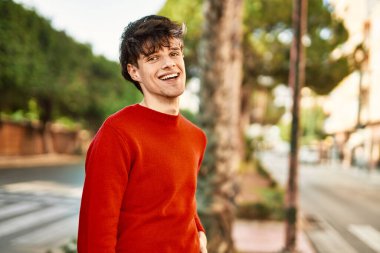 Genç İspanyol adam gülümseyerek şehirde mutlu mesut dikiliyor.