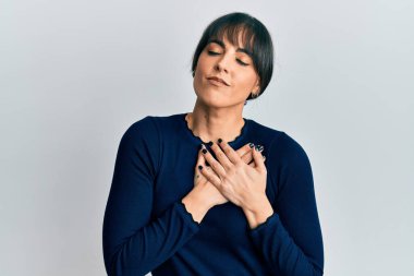 Gündelik kıyafetler giyen genç İspanyol kadın elleri göğsünde gülümsüyor, gözleri kapalı, yüzünde minnet ifadesi var. sağlık kavramı. 