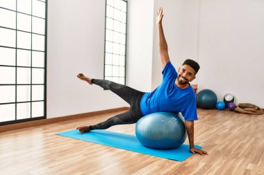 Yakışıklı İspanyol adam egzersiz yapıyor ve yoga minderinde geriniyor, spor salonunda pilates topuyla esneklik gösteriyor.