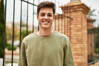 Genç İspanyol adam gülümseyerek şehirde mutlu mesut dikiliyor..