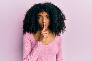 Afro saçlı, pembe gömlekli, dudakları parmaklı Afro-Amerikan bir kadın sessiz olmak istiyor. sessizlik ve gizli konsept. 