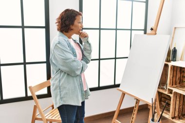 Orta yaşlı İspanyol bir kadın ciddi bir ifadeyle resim stüdyosunda resim çiziyor..