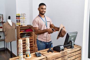 Genç Arap adam giyim mağazasında çalışırken kendinden emin gülümsüyor.