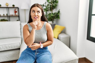 Evdeki kanepede oturan genç esmer kadın bir soru hakkında endişeli ve gergin. 