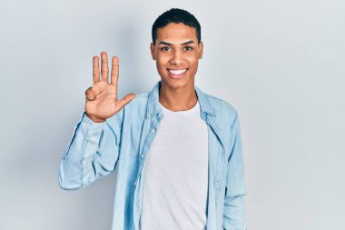 Genç, Afro-Amerikalı, günlük kıyafetler giymiş dört numarayı gösterip işaret ederken kendinden emin ve mutlu bir şekilde gülümsüyor.. 