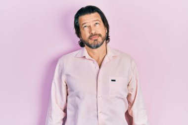 Orta yaşlı, günlük kıyafetler giyen beyaz bir adam. Yüzünde ciddi bir ifadeyle rahatlamış. Basit ve doğal bir şekilde kameraya bakıyorsun.. 