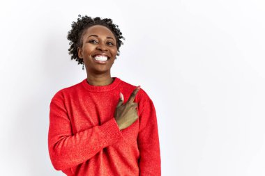Genç Afro-Amerikalı kadın, izole edilmiş arka planda günlük giysiler giyiyor. Neşeli bir şekilde, yüzünde mutlu ve doğal bir ifadeyle, el ve parmak ile yüzünü gösteren bir gülümseme ile. 