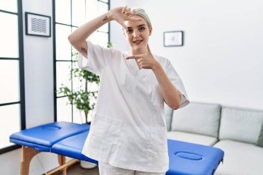 Kafkasyalı genç fizyoterapist kadın evde gülümseyip mutlu yüzlü eller ve parmaklarla çerçeve yapıyor. yaratıcılık ve fotoğrafçılık kavramı. 