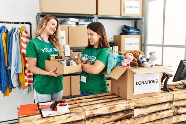 İki genç gönüllü kadın, hayır kurumunda bağışlanacak yiyeceklerle birlikte mutlu bir şekilde kutuda gülümsüyor..