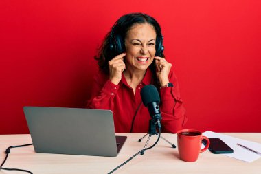 Radyo stüdyosunda çalışan orta yaşlı güzel bir kadın yüksek sesli müzik sesi için parmaklarıyla kulaklarını kapatıyor. sağır kavramı. 