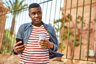 Genç Afrikalı Amerikalı adam akıllı telefon kullanıyor. Şehirde kahve içiyor..