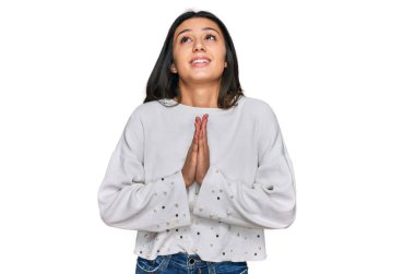 Gündelik giysiler giyen genç İspanyol kız elleri ile yalvarıyor ve dua ediyor. Yüzünde umut ifadesi var. Çok duygusal ve endişeli. Yalvarıyor. 