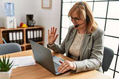 Orta yaş çağrı merkezi ajanının ofisteki bilgisayarı kullanarak görüntülü arama yapması..