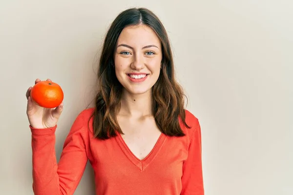 Joven Morena Sosteniendo Naranja Fresca Mirando Positiva Feliz Pie Sonriendo —  Fotos de Stock