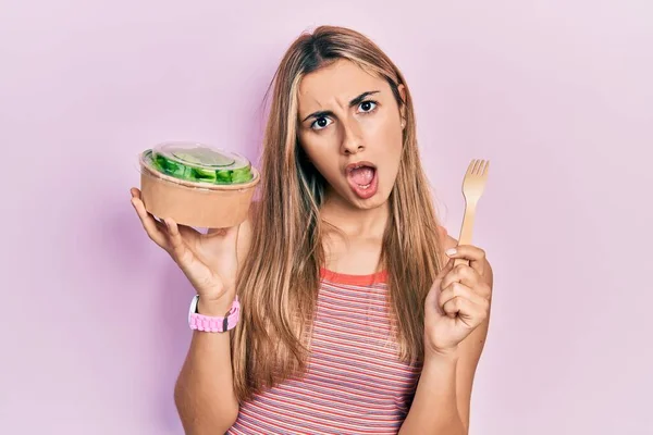 美しいヒスパニック系の女性ショック顔でサラダを食べます 懐疑的で皮肉を探して オープン口で驚いて — ストック写真