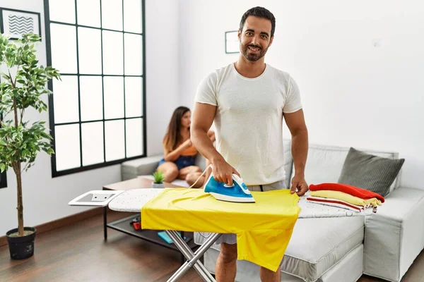 Kadınlar kanepede otururken, erkek gülümseyen mutlu ütü giysileri oturma odasında duruyor..