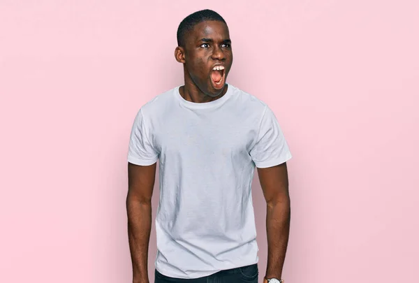 カジュアルな白いTシャツを着た若いアフリカ系アメリカ人の男性は怒りと怒りで叫んで フラストレーションと怒りを叫んで怒っています 怒りと攻撃的な考え方 — ストック写真